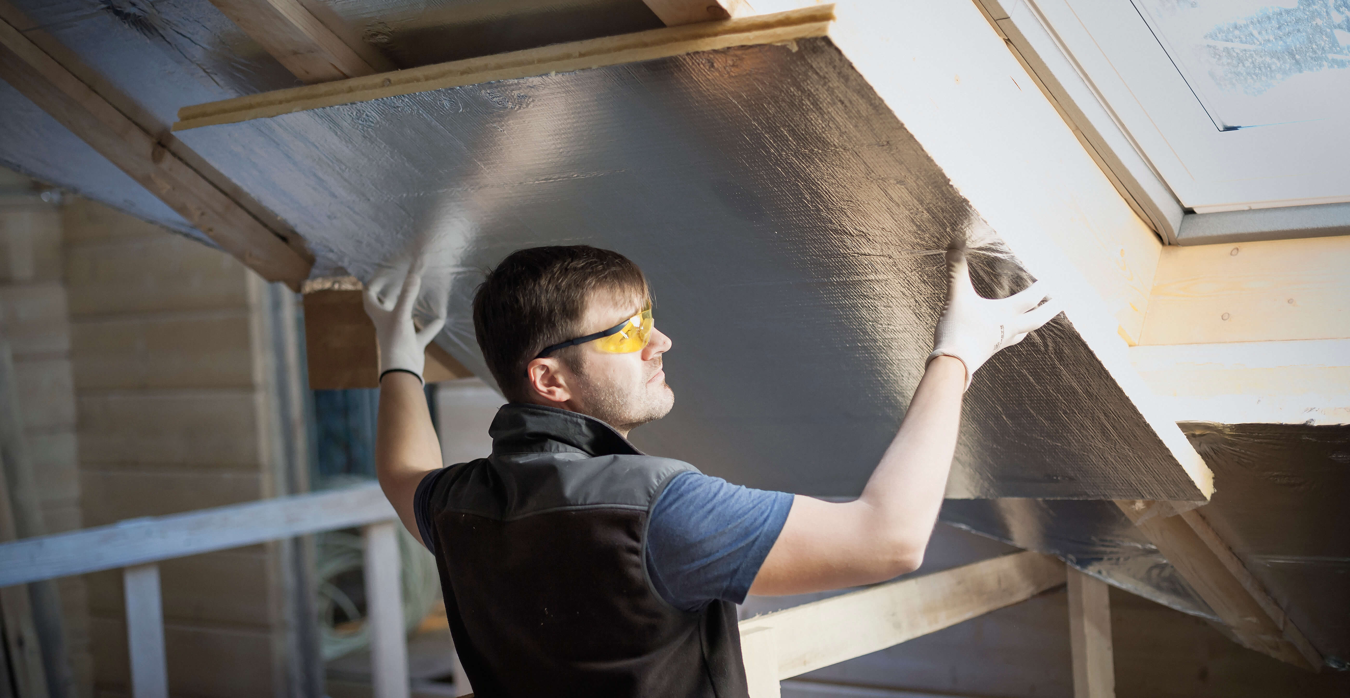 Handyman with protection glasses and white gloves on, insulating a house
