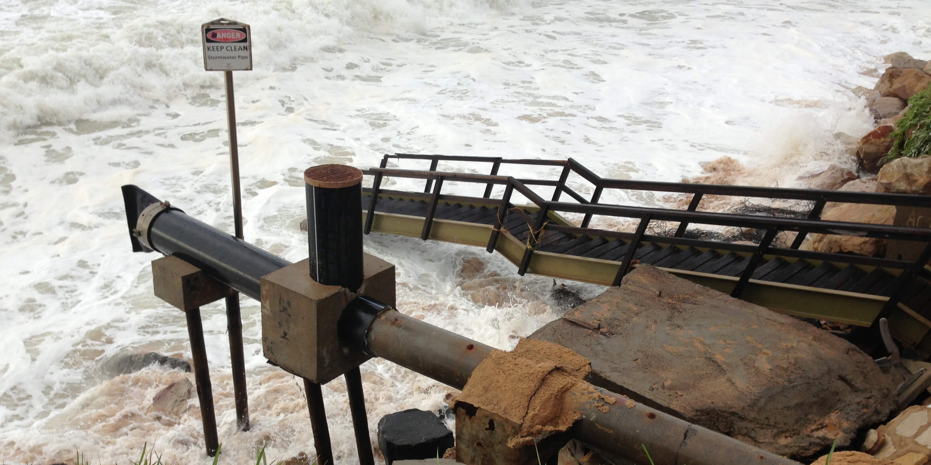 Image of a pipe going from the land to sea with a stormy sea in the background