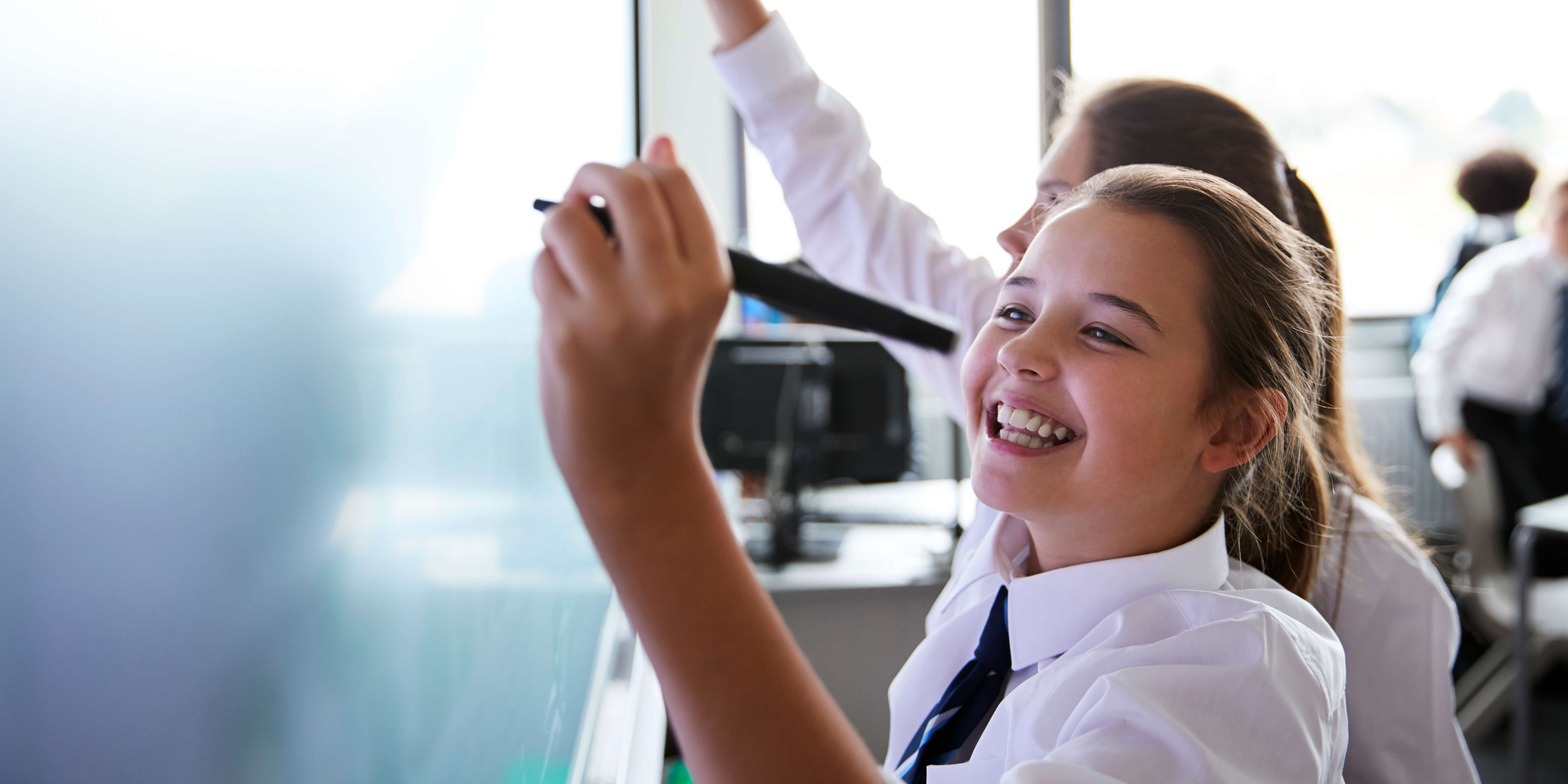 Close up of a girl in school uniform smiling as she writes on an interactive whiteboard