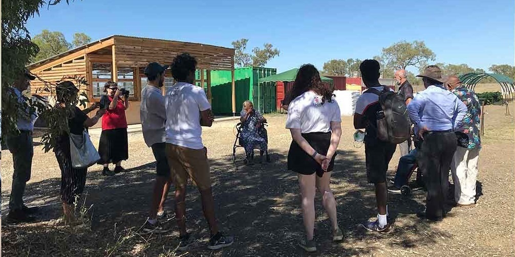 A group of people standing outside in a circle listening to an Elder