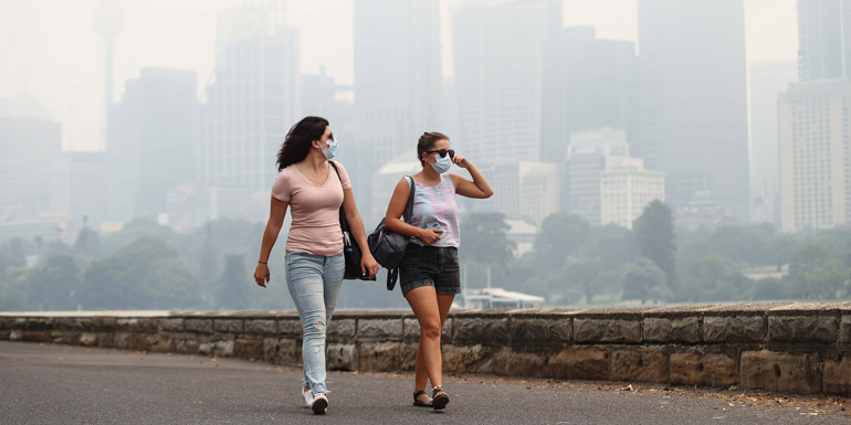 2 women walking with face masks with the Sydney CBD shrouded in haze in the background