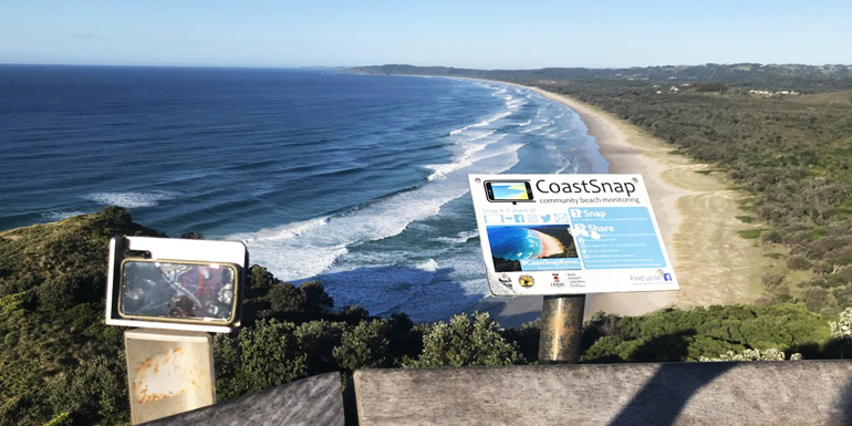 image of a long beach next to bushland with a coastsnap smart phone cradle in the foregound
