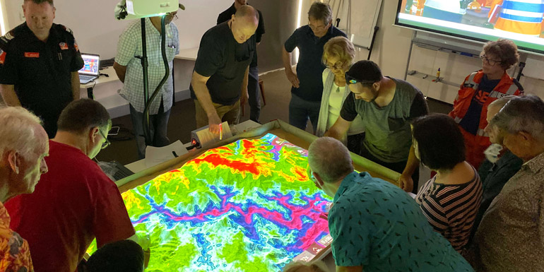 Group of people looking over a large electronic map on a table 