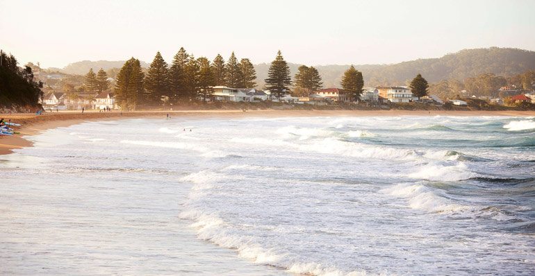 View of a beach with houses, trees and hills with the ocean in the foreground