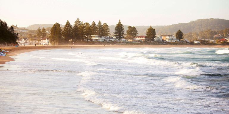 View of a beach with houses, trees and hills with the ocean in the foreground