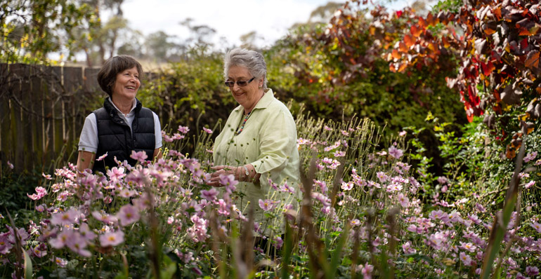 two elderly women laughing in a garden surrounded by flowers