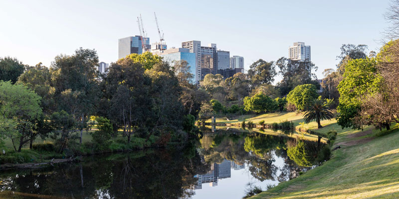 river with parkland either side and some tall buildings in the background