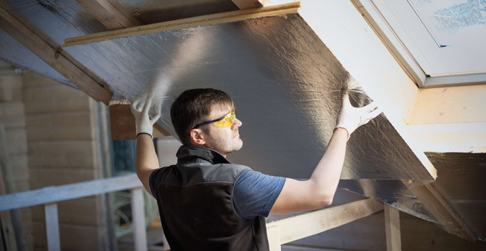 Handyman with protection glasses and white gloves on, insulating a house
