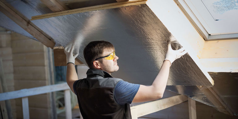 Handyman with protection glasses and white gloves on, insulating a house