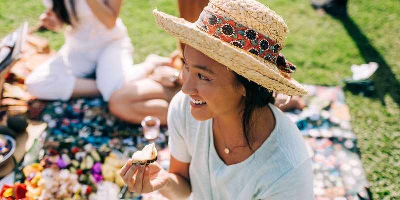 Woman with a hat enjoying some food at a picnic with friends