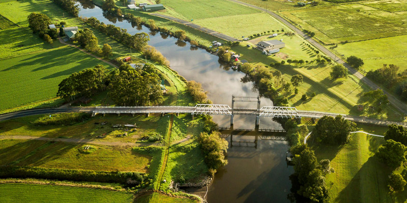 Aerial landscape of a river in the middle of a grassland with a bridge showing the Hunter Valley Flood Mitigation Scheme in NSW