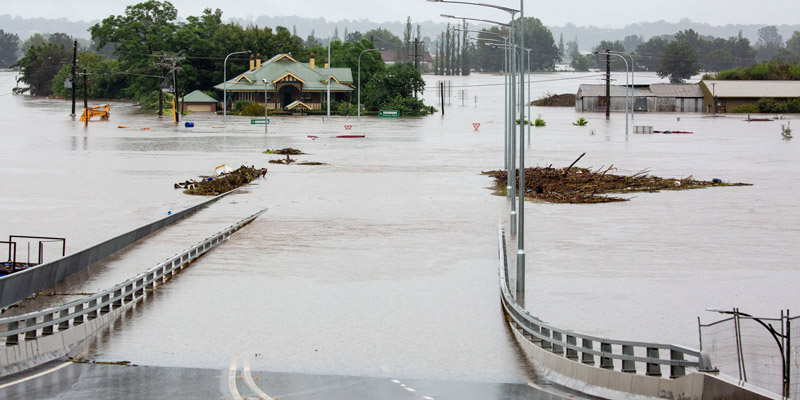 A bridge with a flooded river and debris floating past