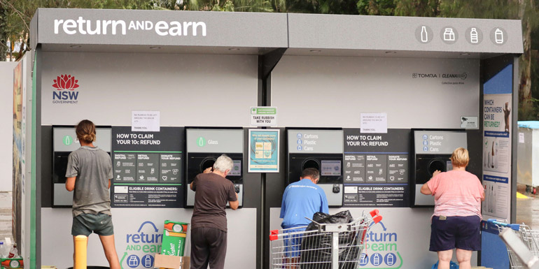Four people seen from behind using a NSW Government Return and Earn Reverse vending machine 