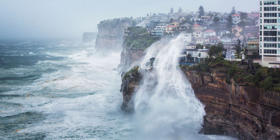 Coastline with habitations close to the edge of a cliff in a stormy weather with an impressive wave splashing up the cliff to the houses