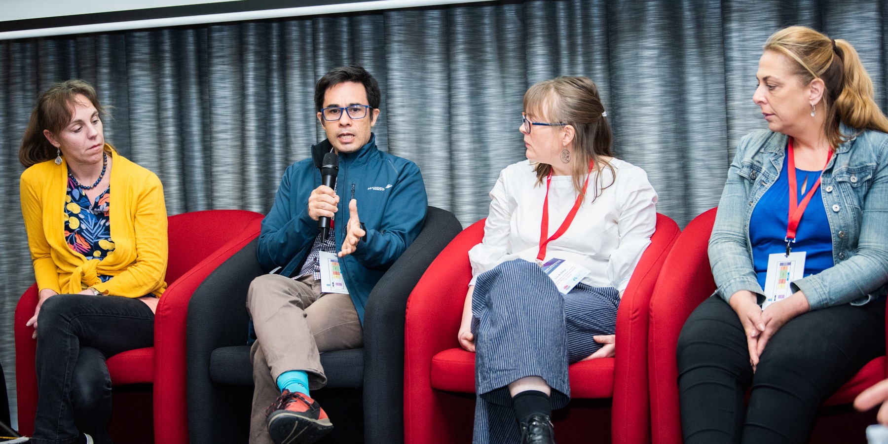 Four people each sitting in chairs speaking at a panel