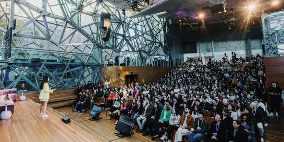 A female is presenting to a crowd of people sitting in an architecturally designed auditorium