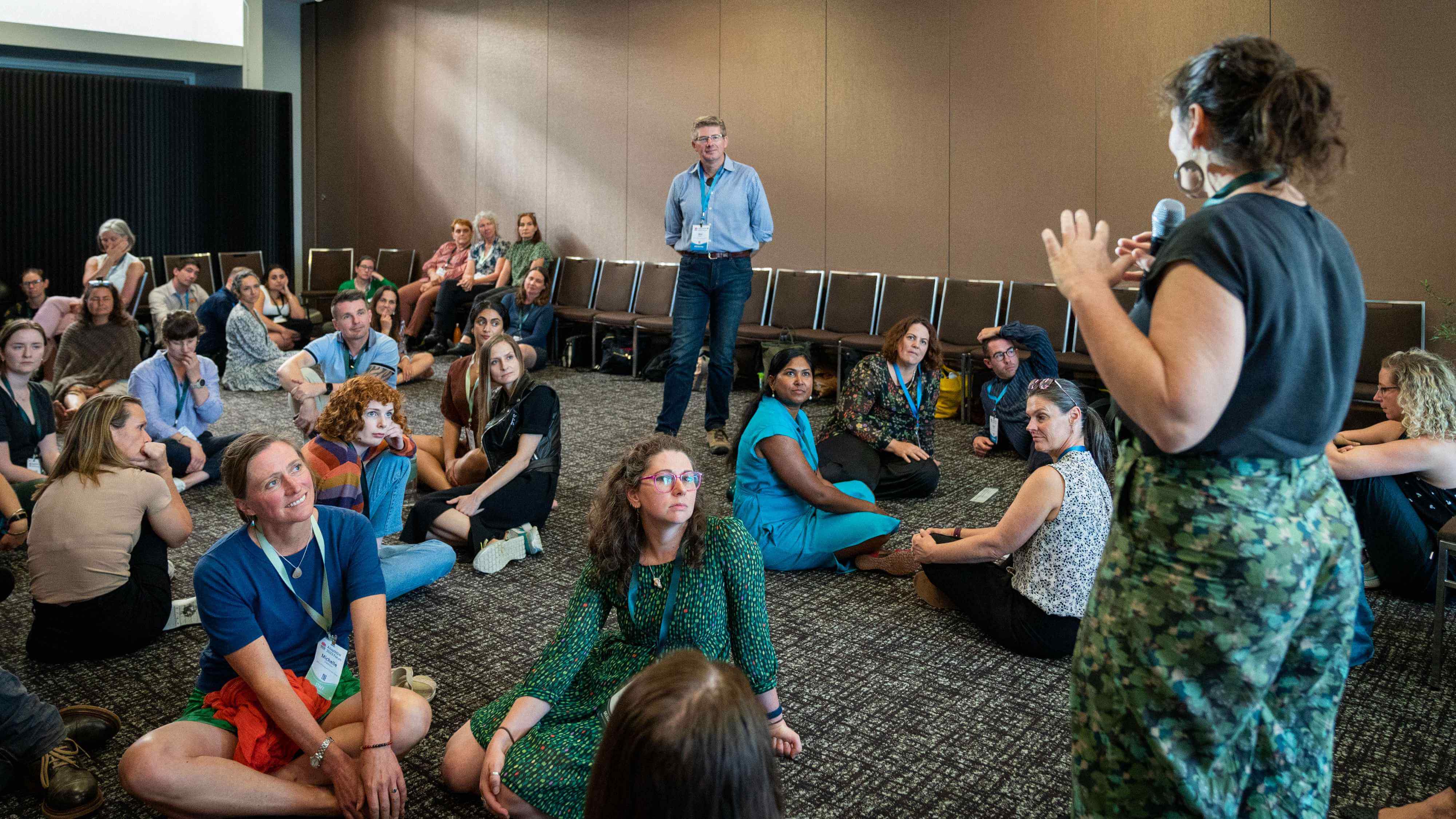 A large group of approximately twenty people sitting on the floor of a room participating in a workshop at the AdaptNSW 20223 Forum. 