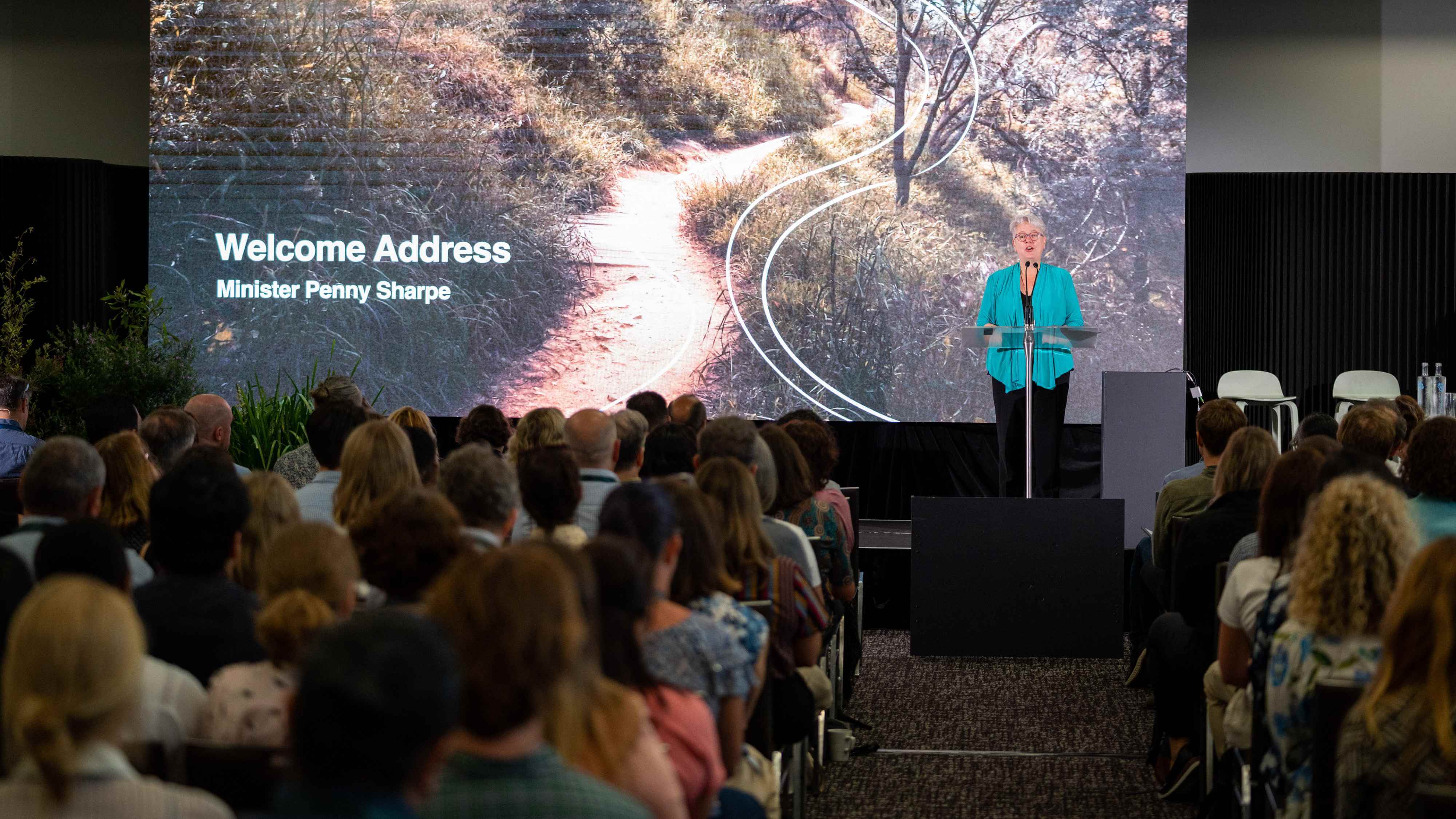 A presenter standing at a podium presenting to a large group of people at the AdaptNSW 2023 Forum.