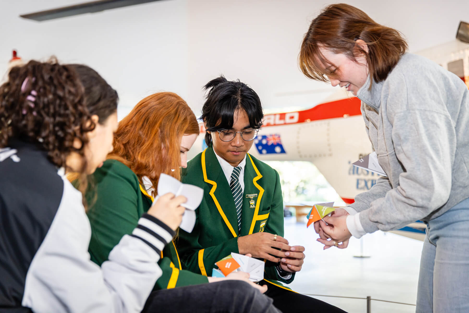 Four high school students sit side by side, smiling and using paper chatterboxes.