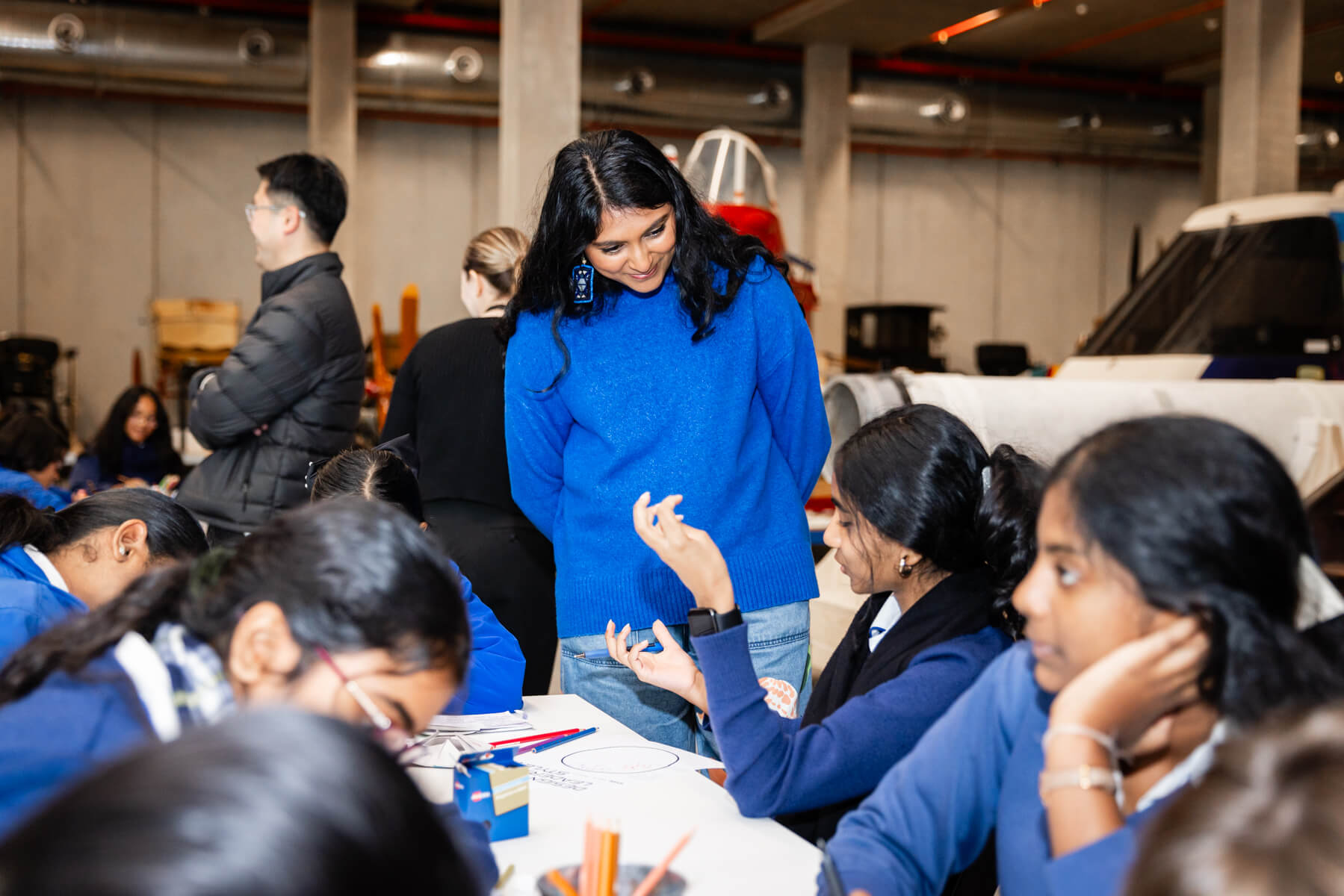 A woman in a blue jumper speaks to high school students amid a workshop.