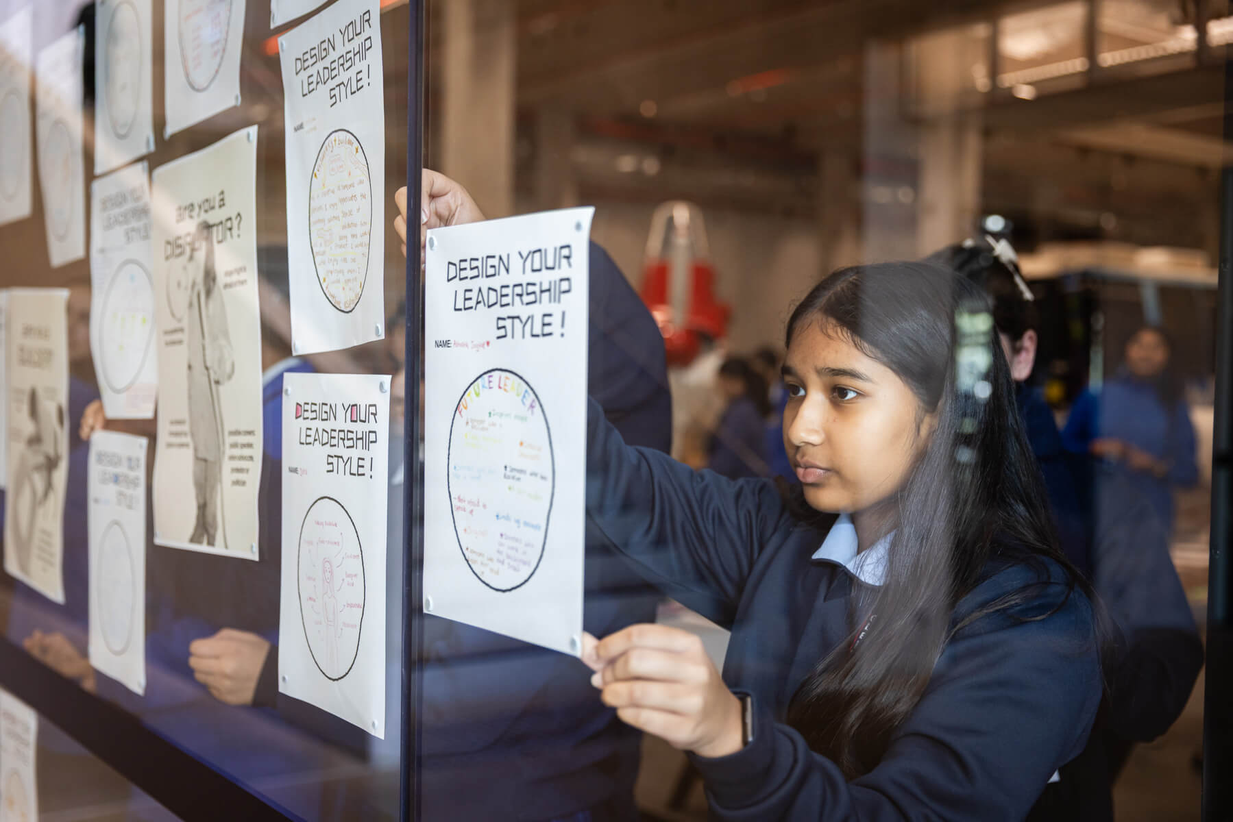 A student affixes her worksheet titled "Design your leadership style" to a glass wall.