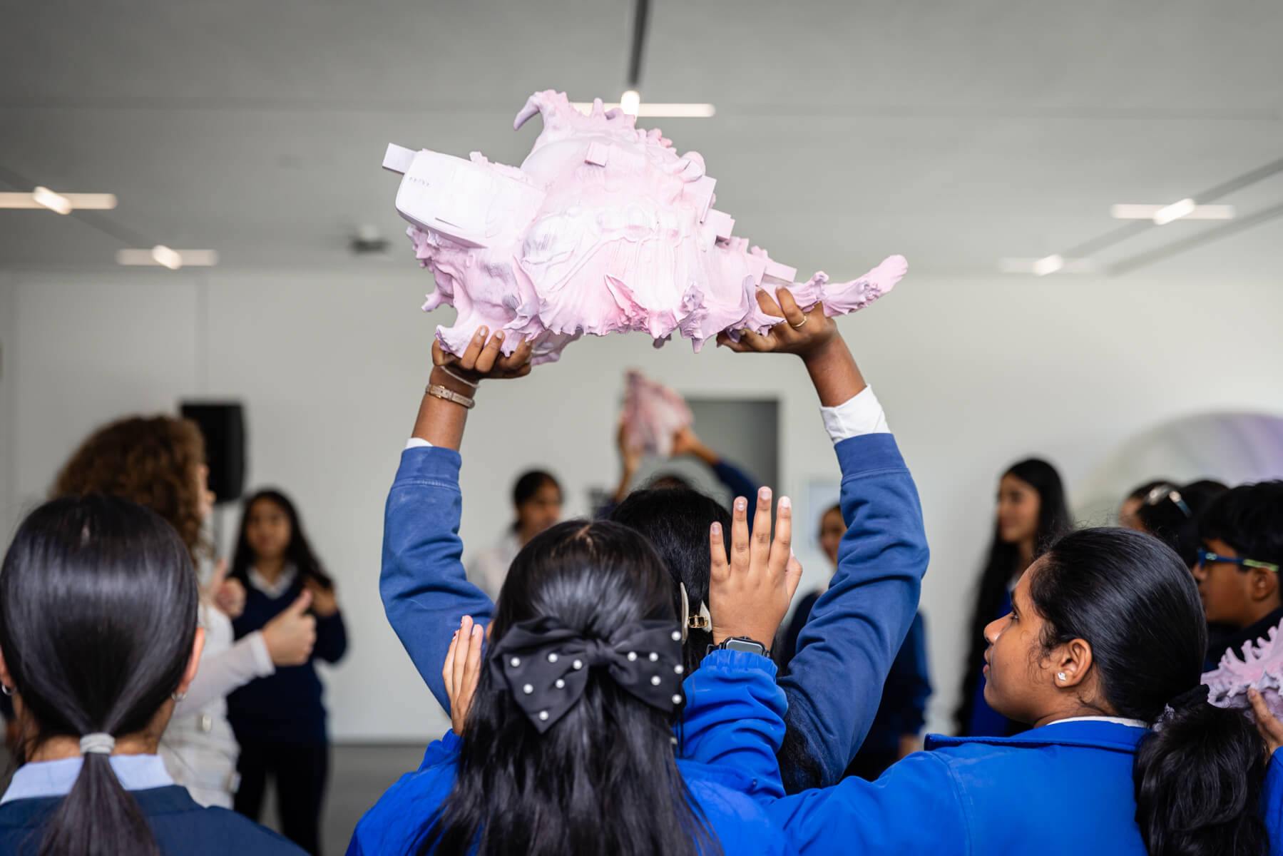 A student is photographed from behind as they stand in a group, holding up a 3D printed shell artwork by Melissa Gilbert.