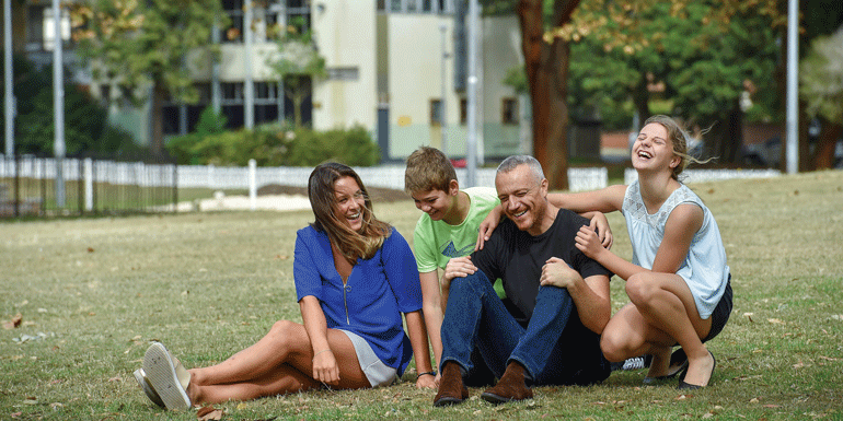 A family relaxing and laughing on the grass in Arncliffe Park, Arncliffe, NSW.