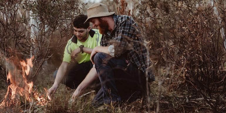 To men crouching next to a fire