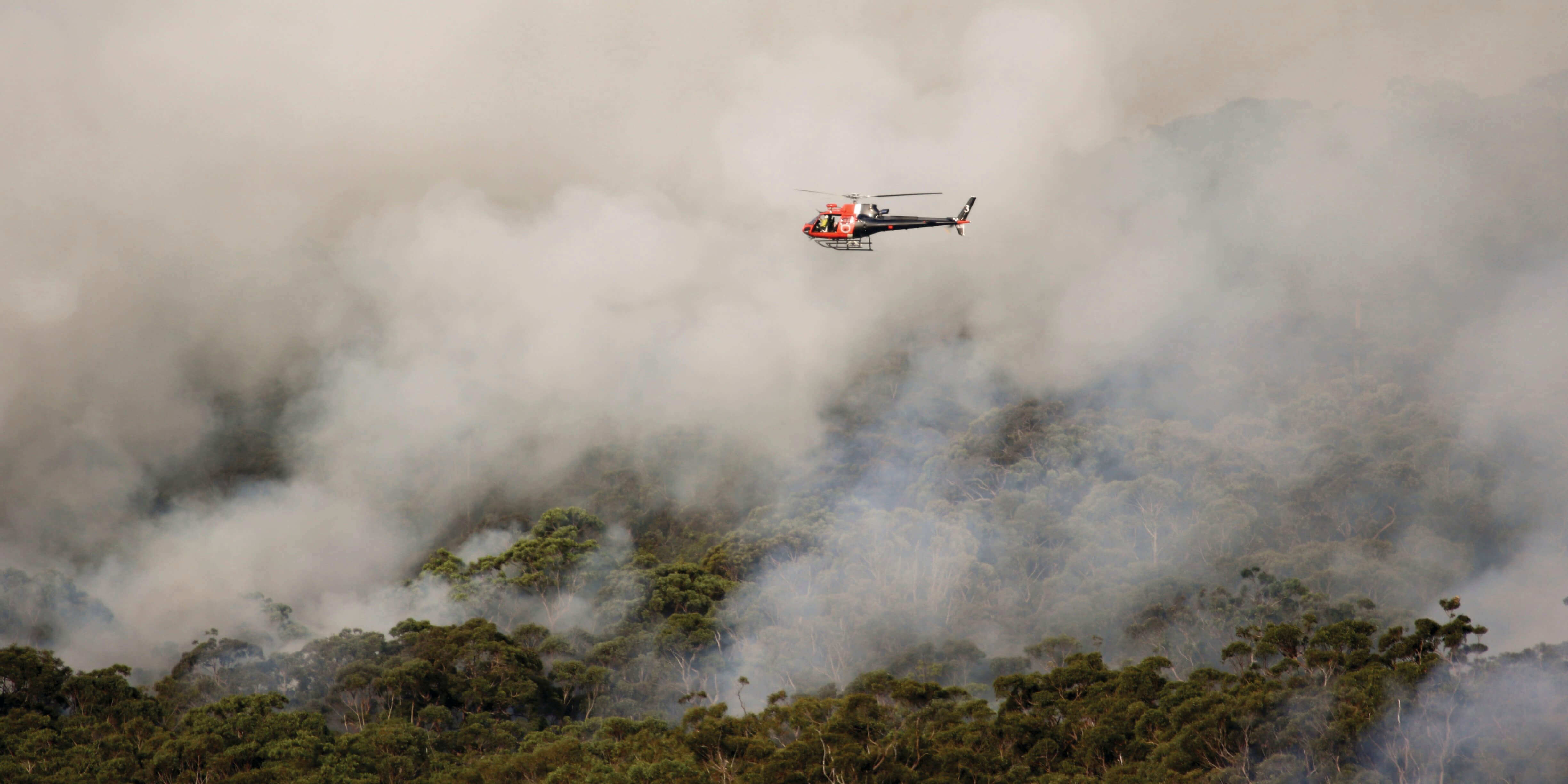 Helicopter flying through smoke above a bushfire