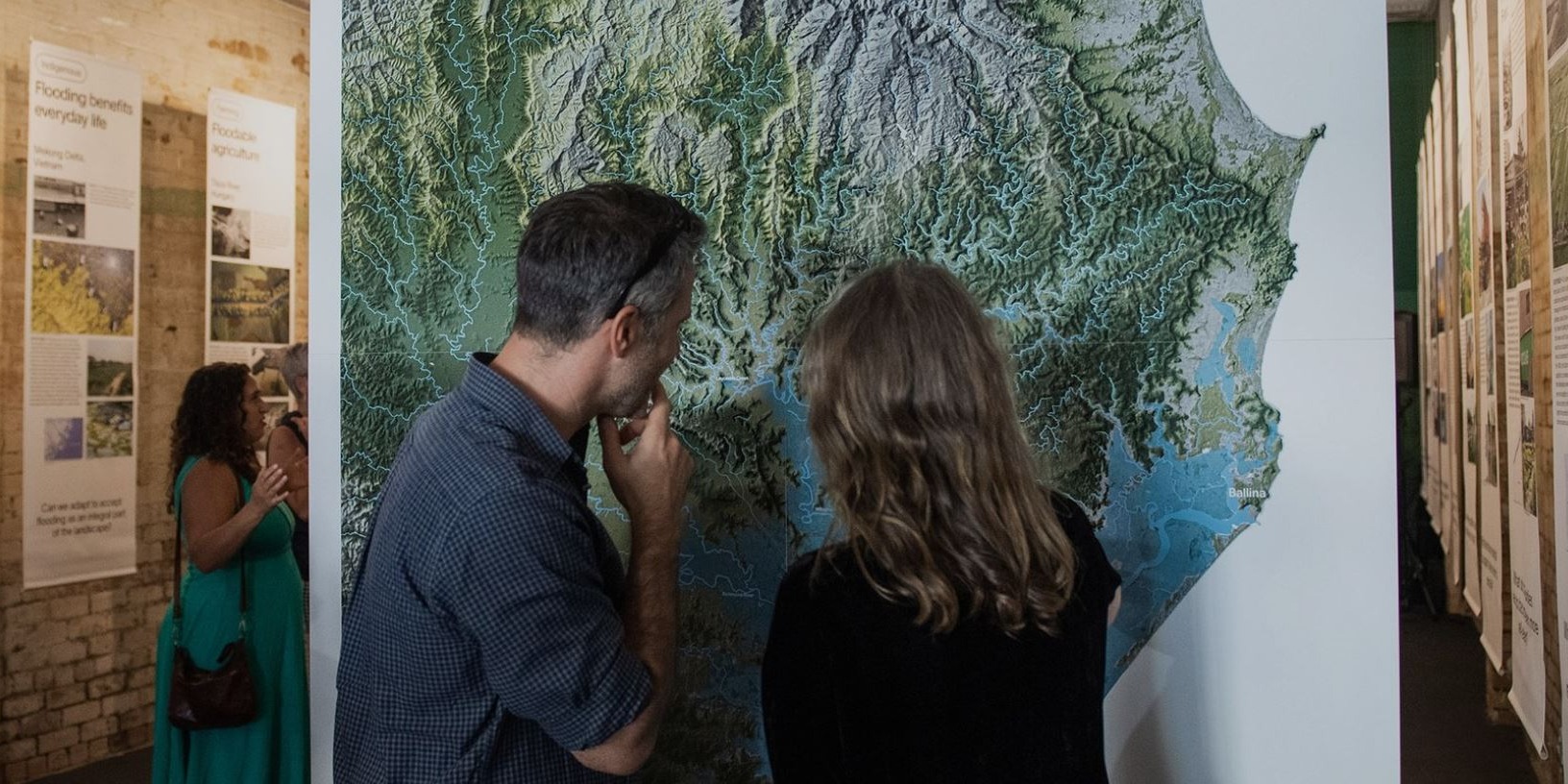 Two people looking at a topography map mounted on a wall.