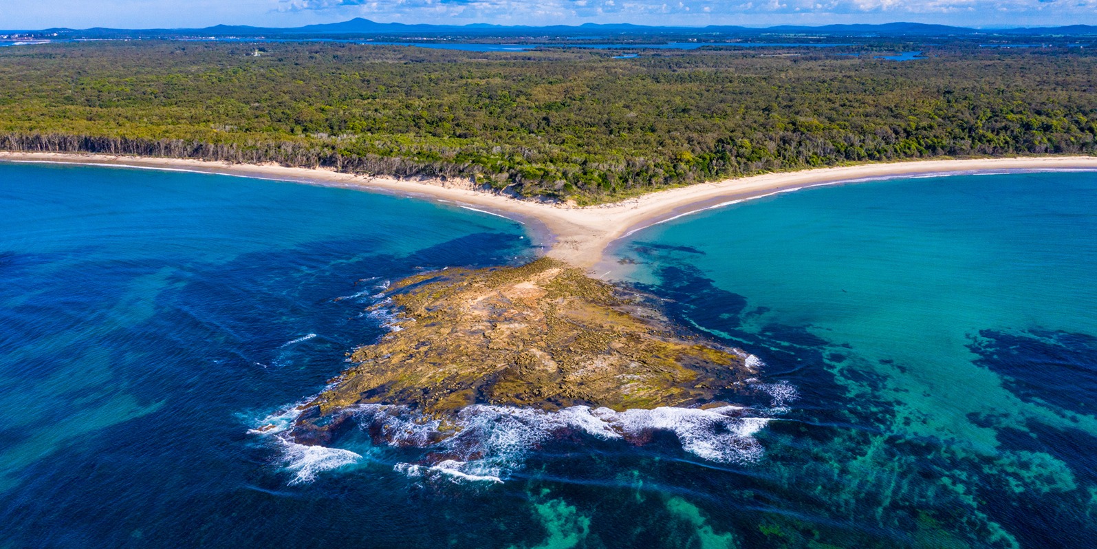 Aerial view of a coastline and far reaching bush land. 