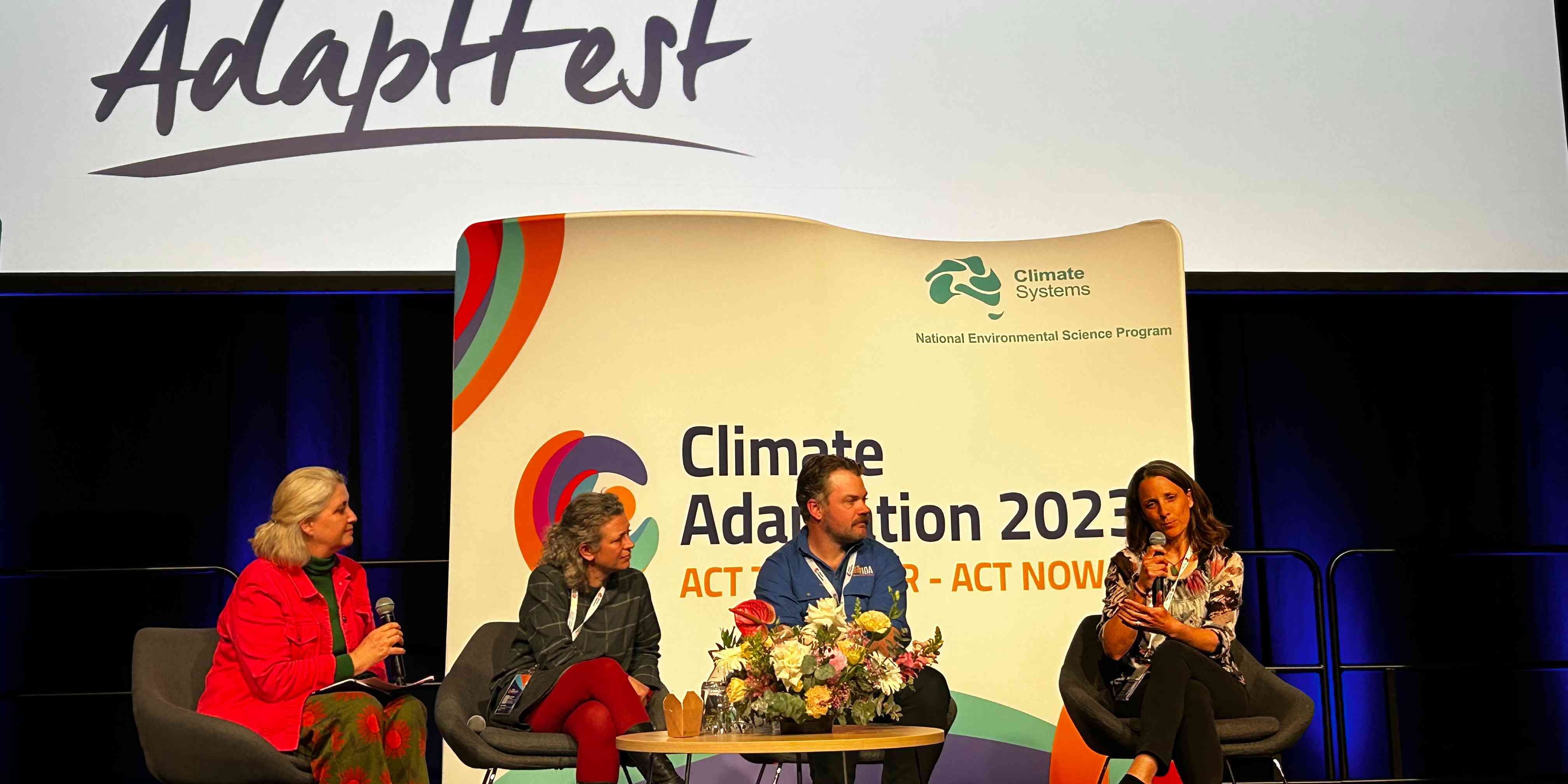 Panel members up stage with a large presentation screen in the background. 